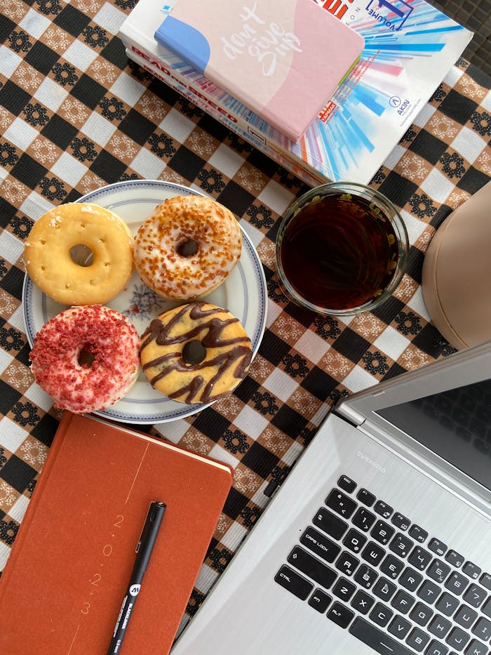 services-04 Four donuts on a plate with iced coffee beside a laptop on a checkered table.