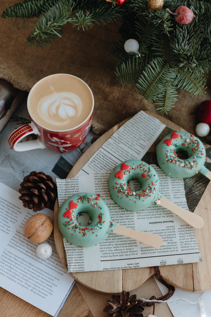 Festive green donuts with holiday decor beside cappuccino, ideal for Christmas celebrations.