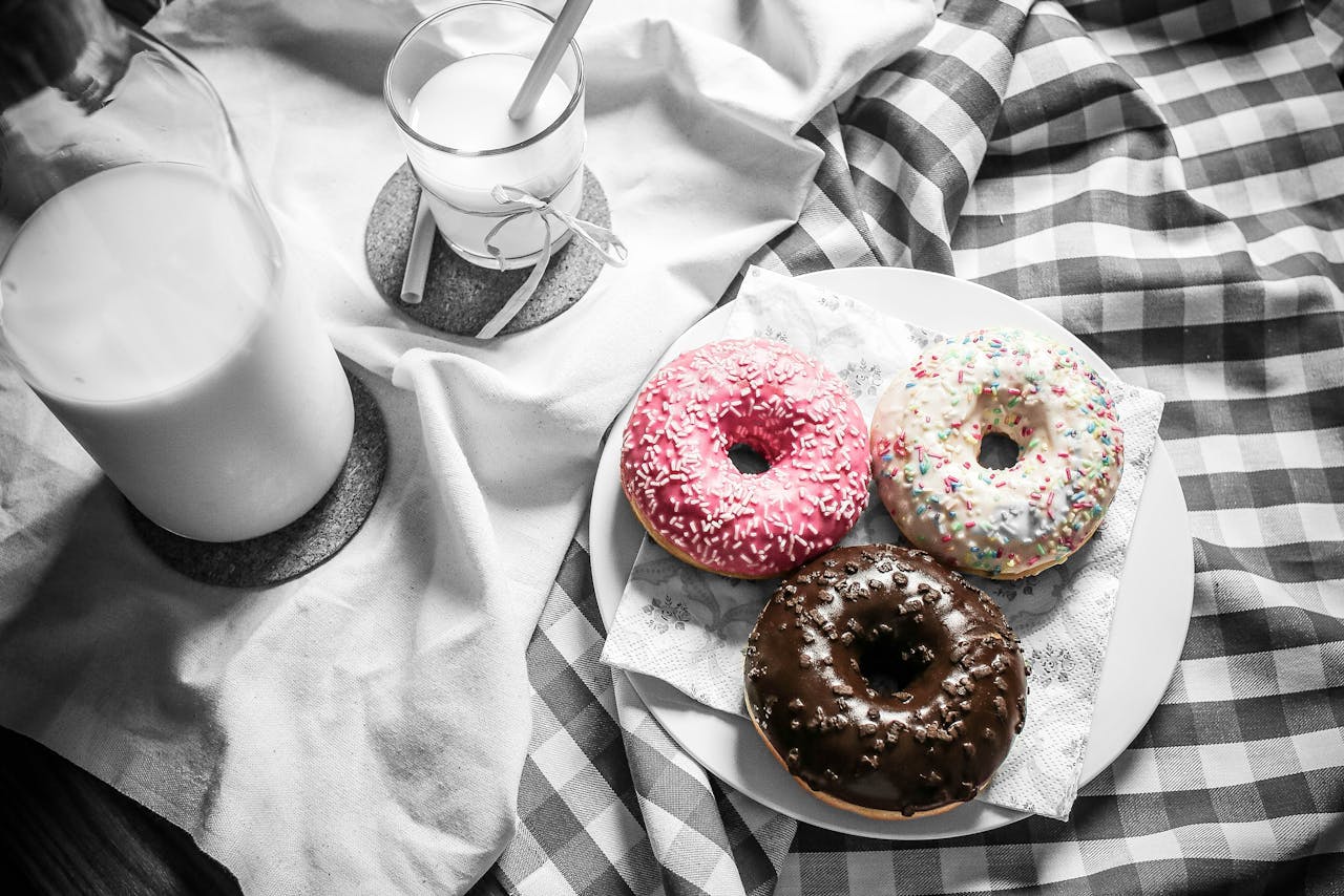 services-03 Three vibrant donuts with milk on a checkered cloth, creating a delightful food scene.