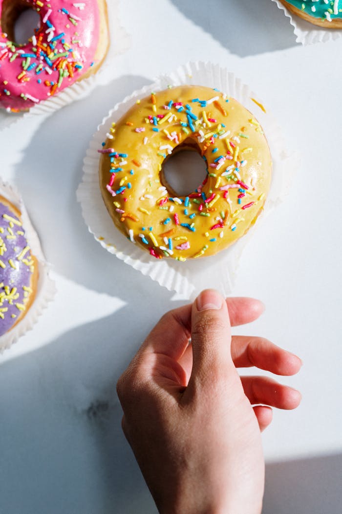 services-03 Close-up of a vibrant donut with colorful sprinkles being picked up, perfect for dessert and food themes.