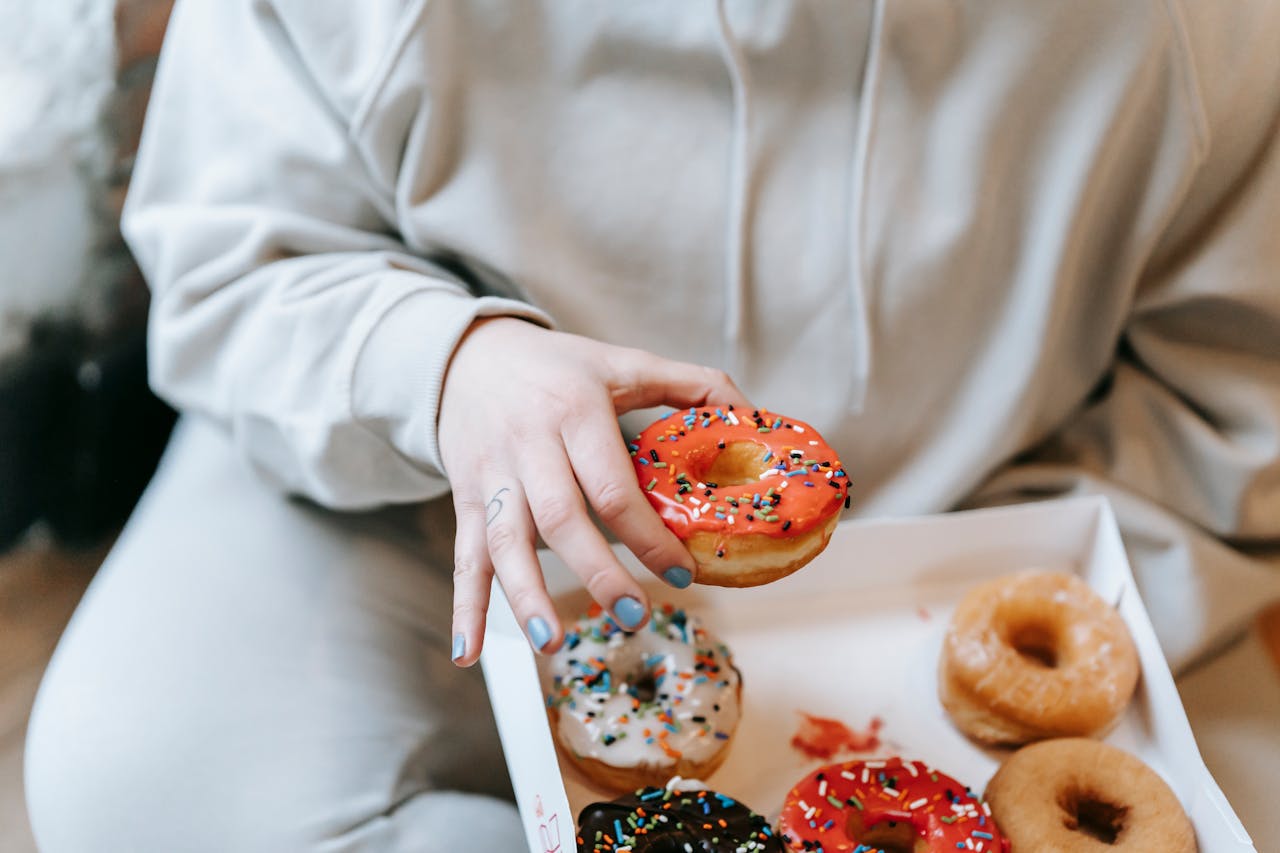 gallery-6 A person enjoying a variety of colorful donuts with sprinkles in a cozy indoor setting.