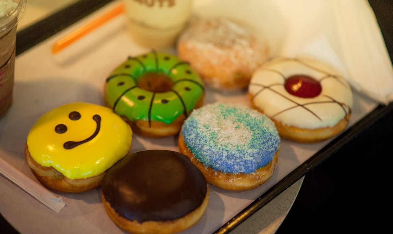 gallery-1 A delicious assortment of colorful and decorated donuts displayed on a bakery tray.