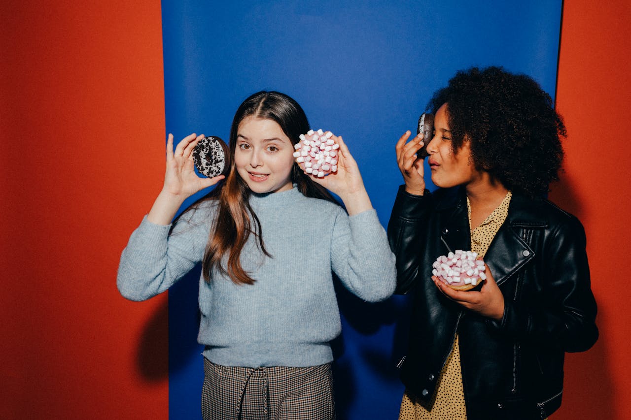 Two teens having fun with donuts in front of a colorful backdrop, expressing happiness.