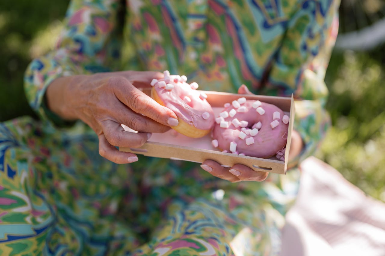 gallery-5 Close-up of a woman holding pink donuts at a picnic with floral attire.