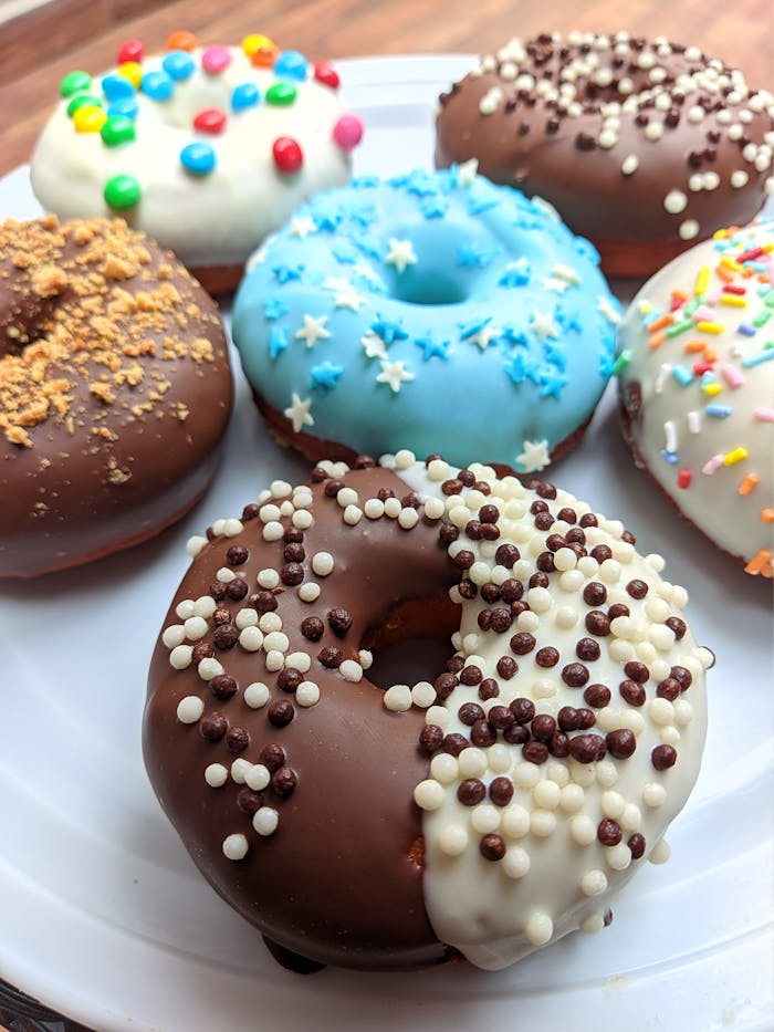 gallery-2 A vibrant assortment of decorated donuts with chocolate glaze and sprinkles, perfect for dessert lovers.